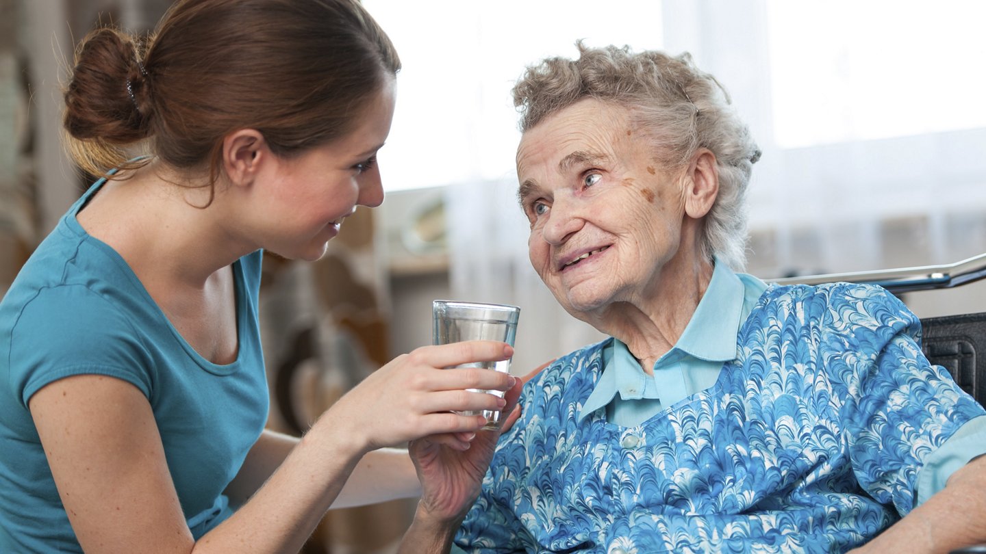 Pflegerin gibt alter Frau eine Glas Wasser
