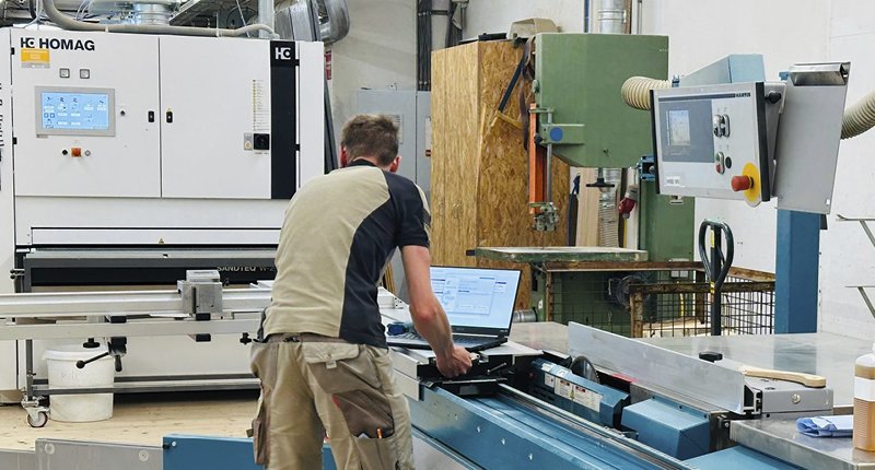 Mitarbeiter wartet mithilfe eines Laptops eine Holzbearbeitungsmaschine in einer Werkstatt.