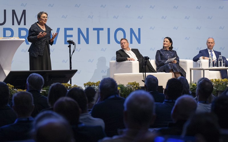 Eröffnung des Forums Prävention 2026 in Innsbruck mit Keynote-Speakerin Elisabeth Oberzaucher am Stehpult und drei weiteren Personen auf der Bühne.
