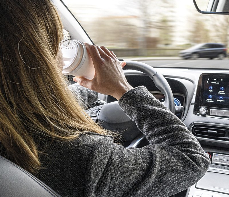 eine Autofahrerin, die aus einem Cafebecher trinkt