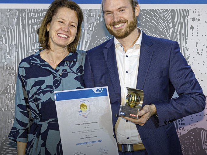 eine Frau und ein Mann mit einer Urkunde bzw. einem Pokal in der Hand freuen sich