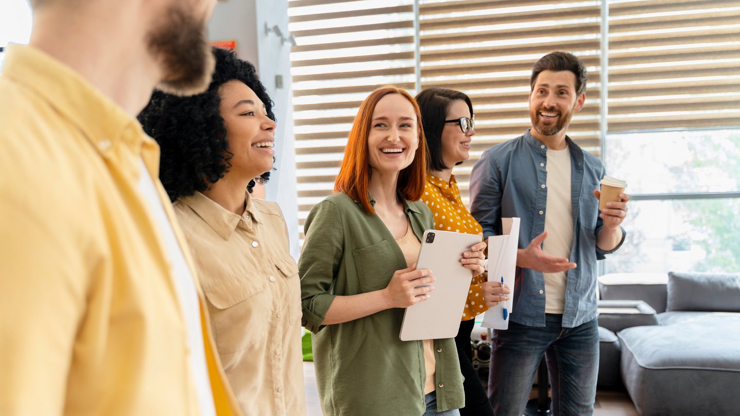 Ein Gruppe von Arbeitnehmer:innen steht im Büro und lacht