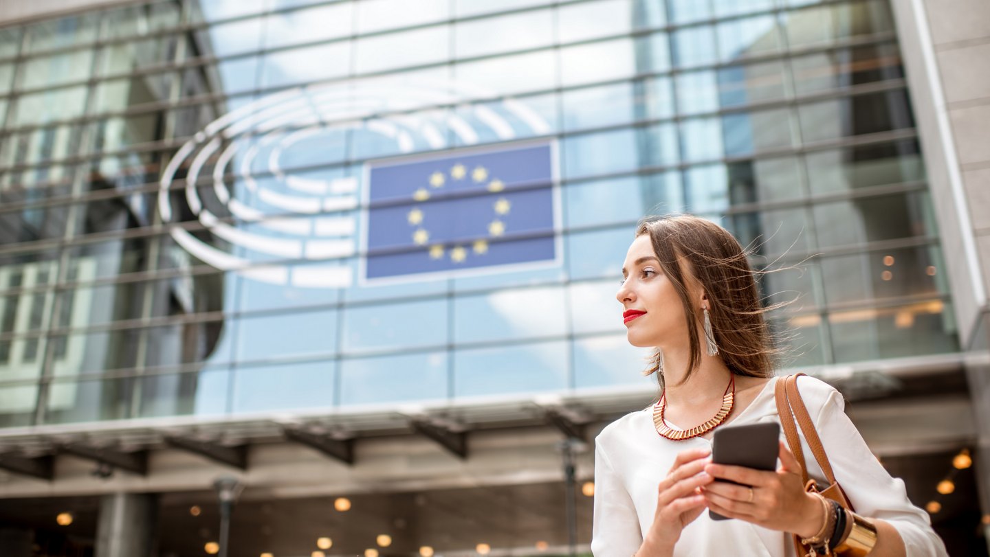 Junge Frau mit Handy in der Hand steht vor dem EU-Parlamant