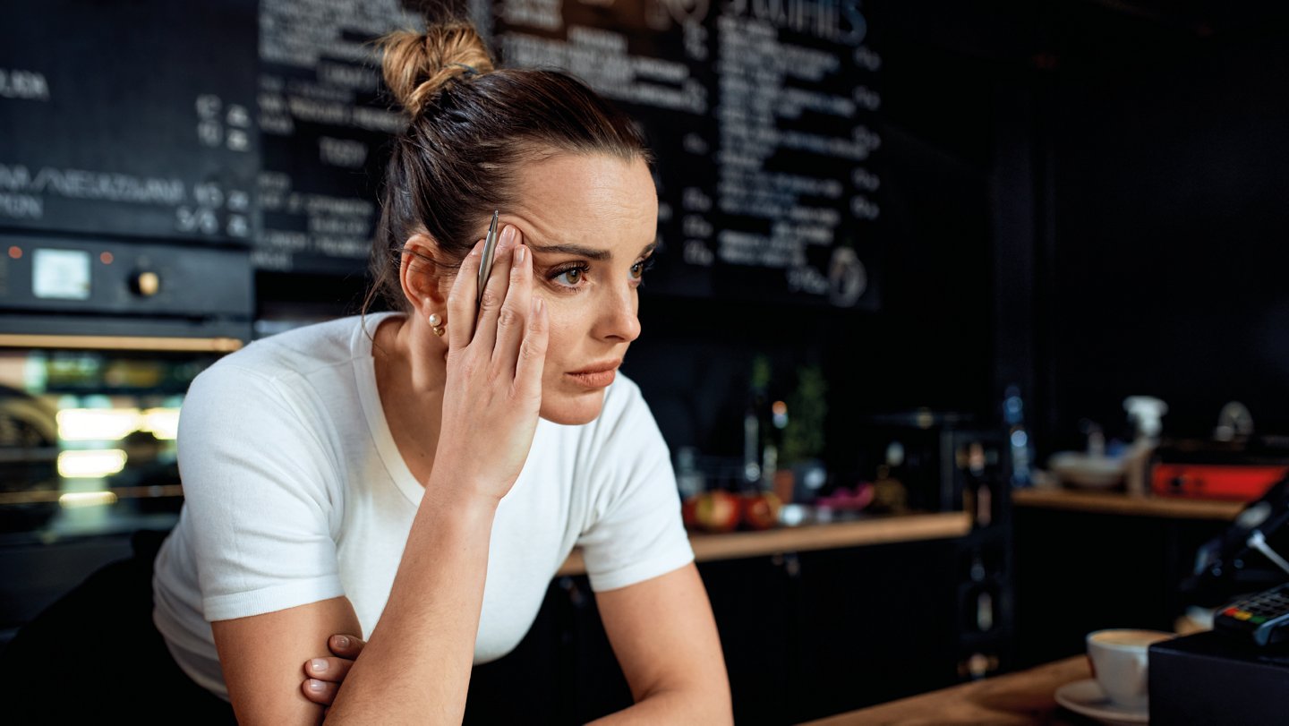 Arbeitnehmerin mit nachdenklichem Blick an der Theke lehnend