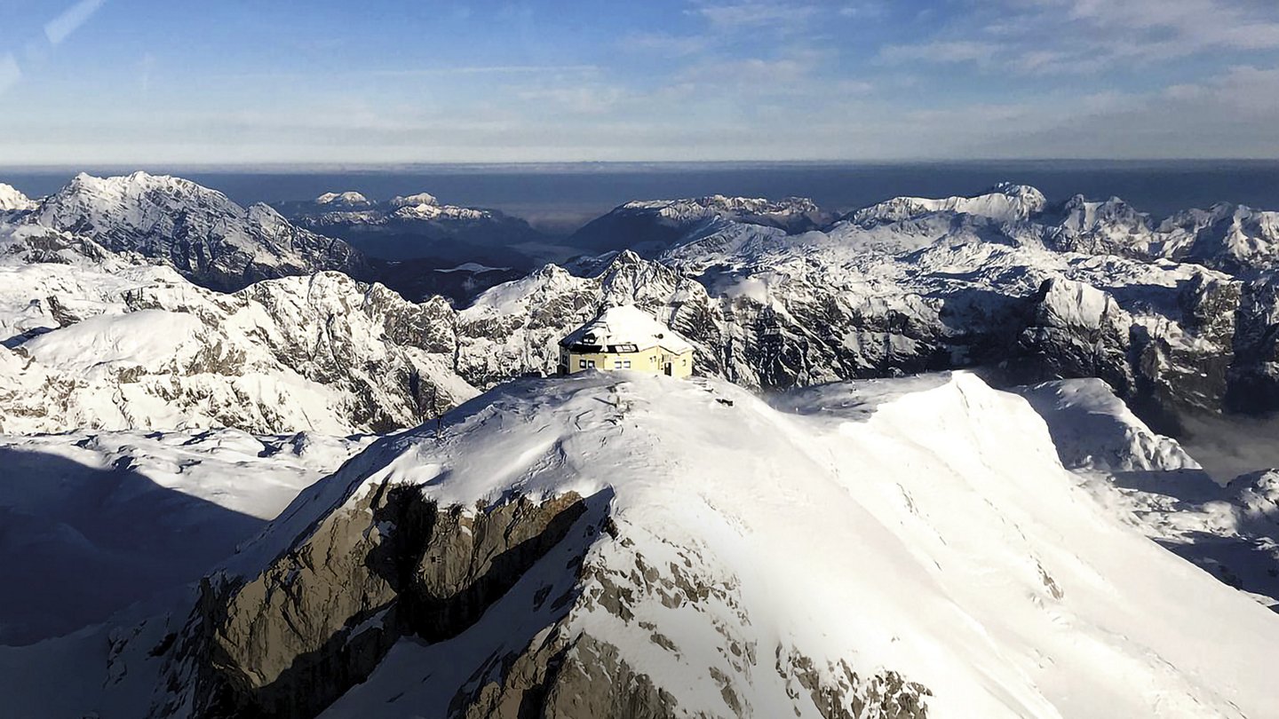 Blick auf schneebedeckte Berge, auf einem Gipfel befindet sich eine Hütte