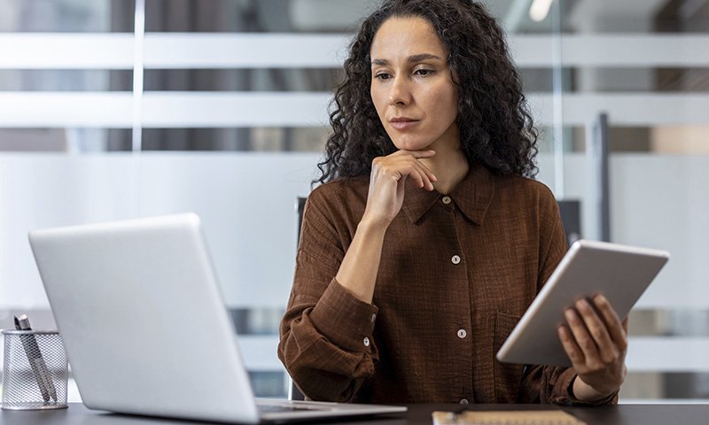 Frau arbeitet konzentriert mit Laptop und Tablet an einem Schreibtisch – symbolisiert digitale Arbeitsmittel im Büroalltag