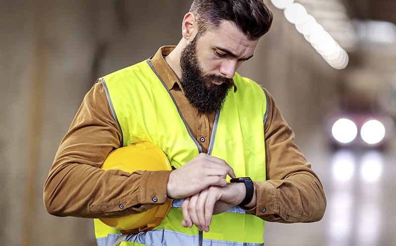 Bauarbeiter mit Warnweste blickt auf seine Smartwatch – symbolisiert Wearables als neue Arbeitsmittel