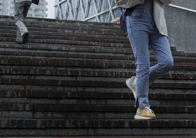 Zwei Personen gehen eine nasse, rutschige Treppe in einer urbanen Umgebung hinauf bzw. hinunter. Eine Person trägt eine helle Jacke und Jeans, die andere eine dunkle Hose. Im Vordergrund ist ein Text über die erhöhte Sturzgefahr in der dunklen Jahreszeit zu sehen.