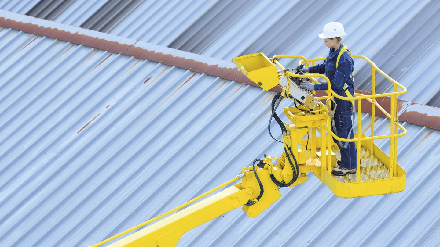 eine Arbeiterin in Schutzkleidung und mit Helm steuert eine Hubarbeitsbühne