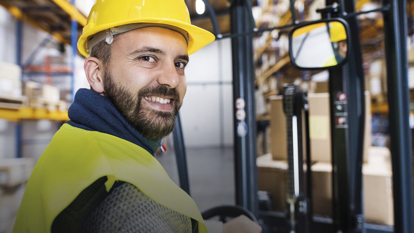 ein Mann mit Helm und Schutzweste sitzt in einem Gabelstapler