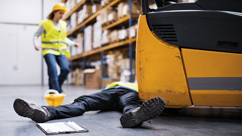 ein verunfallter Mann liegt vor einem Gabelstapler, eine Arbeiterin eilt herbei