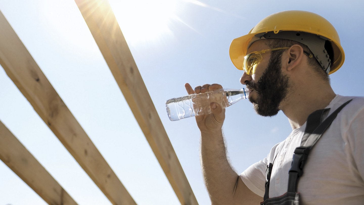 ein Arbeiter auf einer Baustelle trinkt aus einer Wasserflasche