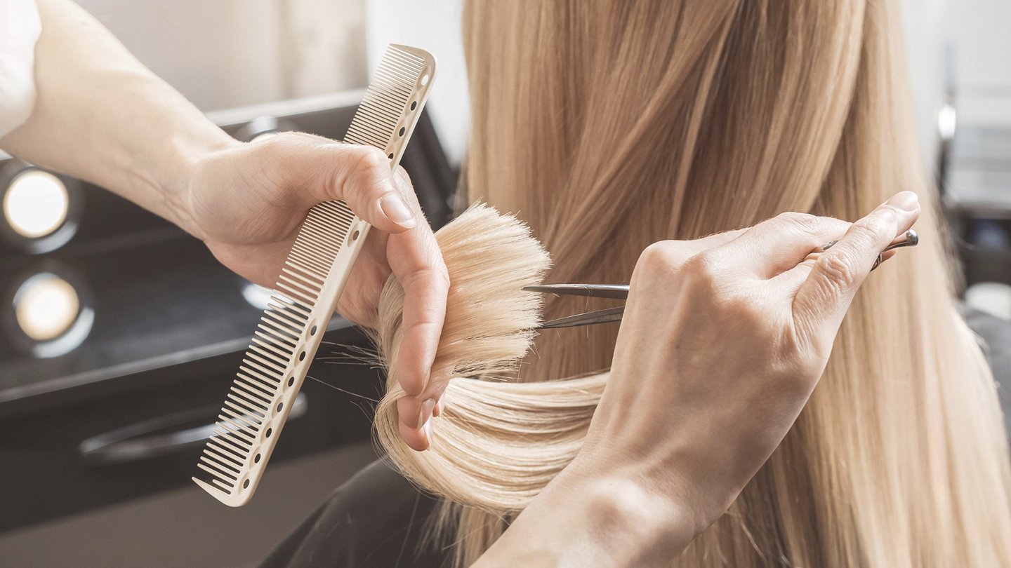 Detailaufnahme zweier Hände, die einer blonden Frau die Haar schneiden