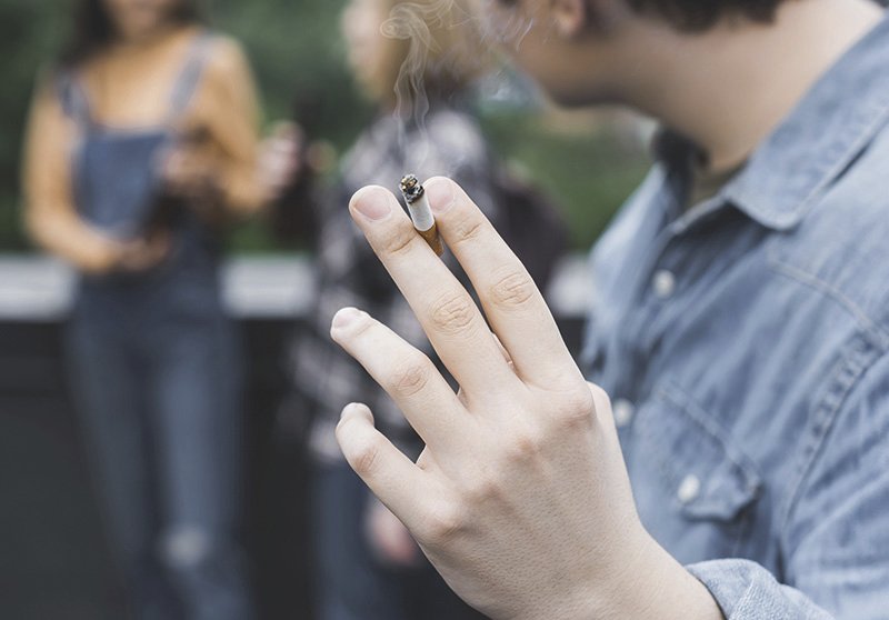 Ein Mann hält eine Zigarette in der Hand und steht Abseits von einigen Personen