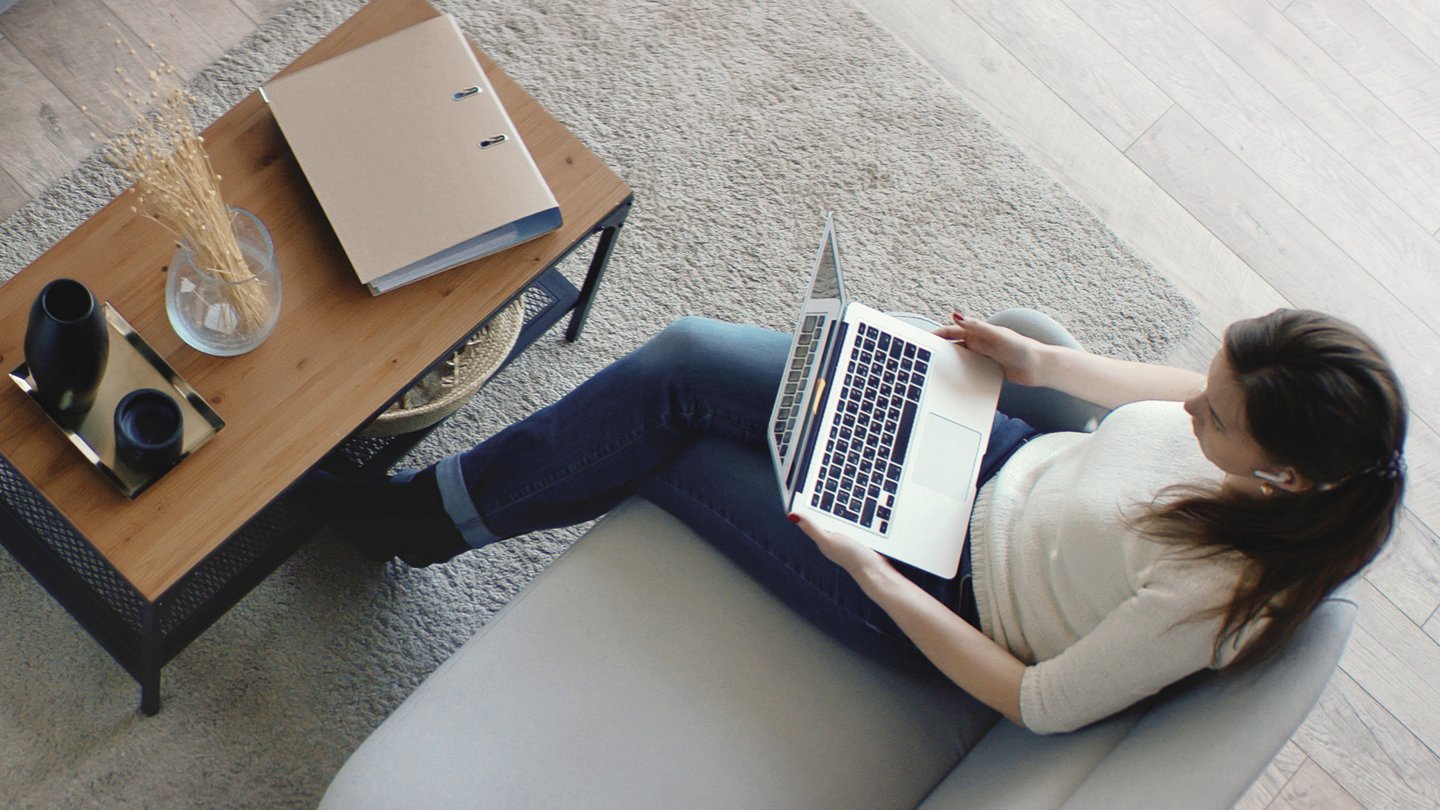 eine Frau sitzt mit Headset und Notebook im Wohnzimmer, am Tisch liegt ein Ordner