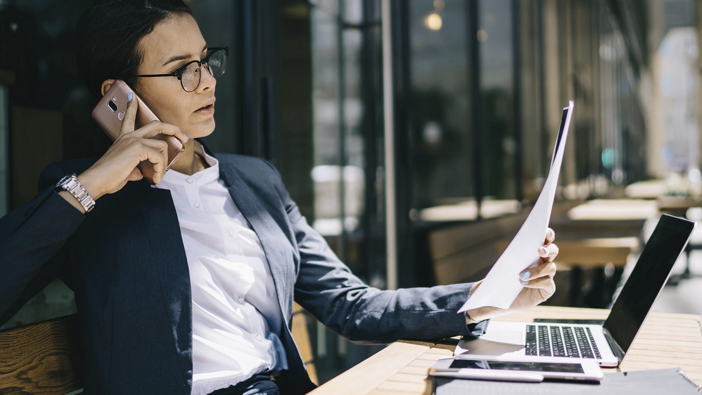 eine Frau sitzt telefonierend vor Ihrem Notebook und hält einen Zettel in der Hand