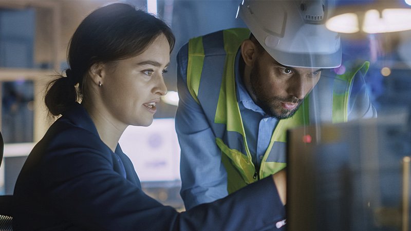 eine Frau und ein Mann blicken in einen Monitor, die Frau erklärt etwas