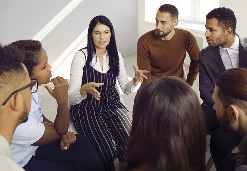 eine Gruppe von Menschen sitzen rund um eine Frau, die etwas erklärt