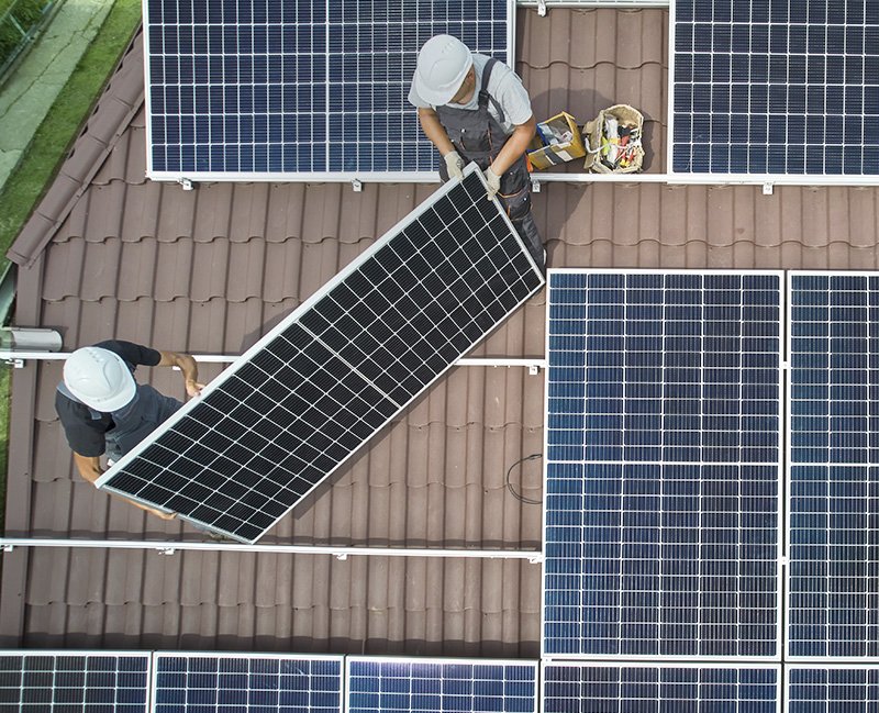 Men workers installing photovoltaic solar moduls on roof of house. Engineers in helmet building solar panel system outdoors. Concept of alternative and renewable energy. Aerial view.