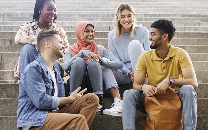 Junge Menschen verschiedenster Herkunft sitzen in fröhlicher Stimmung auf einer Stiege beisammen