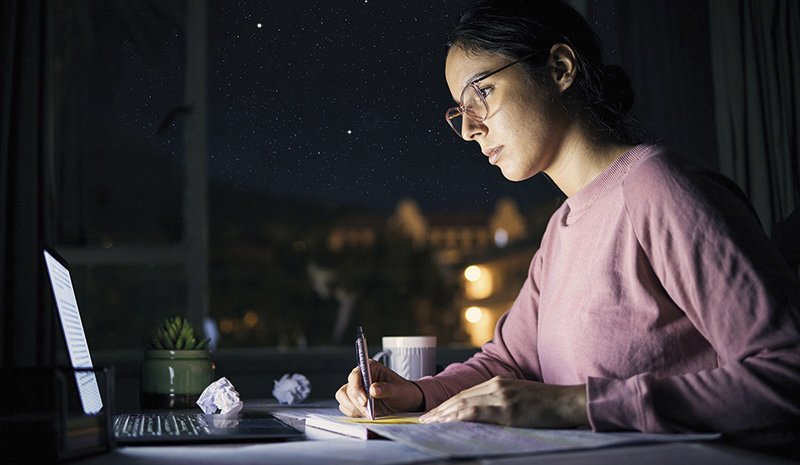 eine Frau sitzt nachts an einem Schreibtisch und arbeitet am Computer