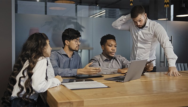 eine Gruppe von jungen Menschen sitzen um ein Notebook herum und besprechen sich angeregt.