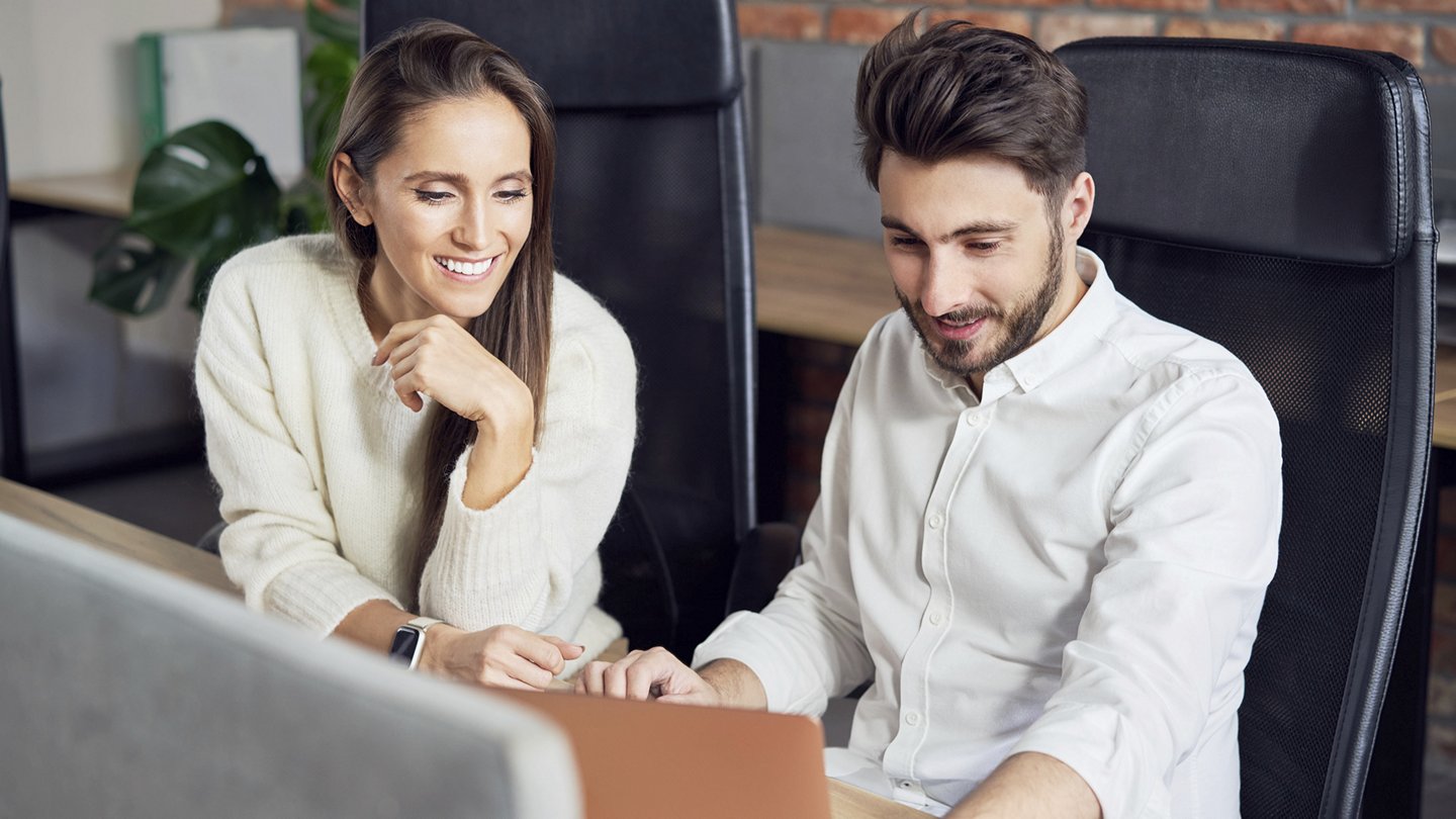 eine Frau und ein Mann sitzen lächelnd nebeneinander und blicken in einen Computer