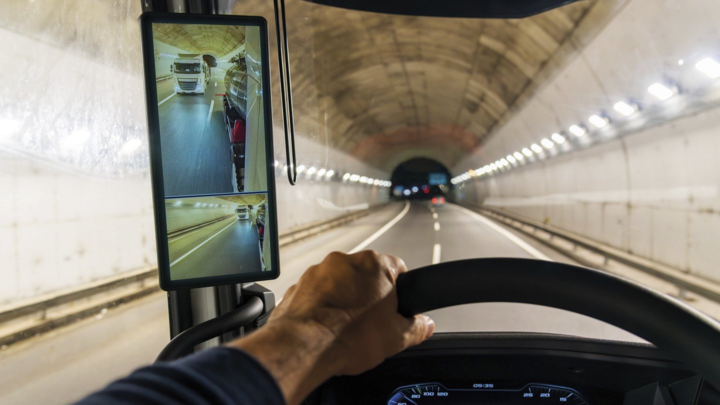 ein Auto fährt durch einen Tunnel, links sieht man einen großen Bildschirm, der einen überholenden LKW zeigt