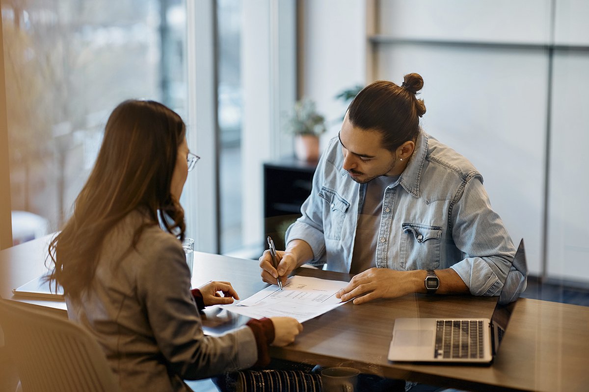 Young Hispanic man signing loan agreement during meeting with his bank manager in office., Young Hispanic man signing loan agreement during meeting with hi