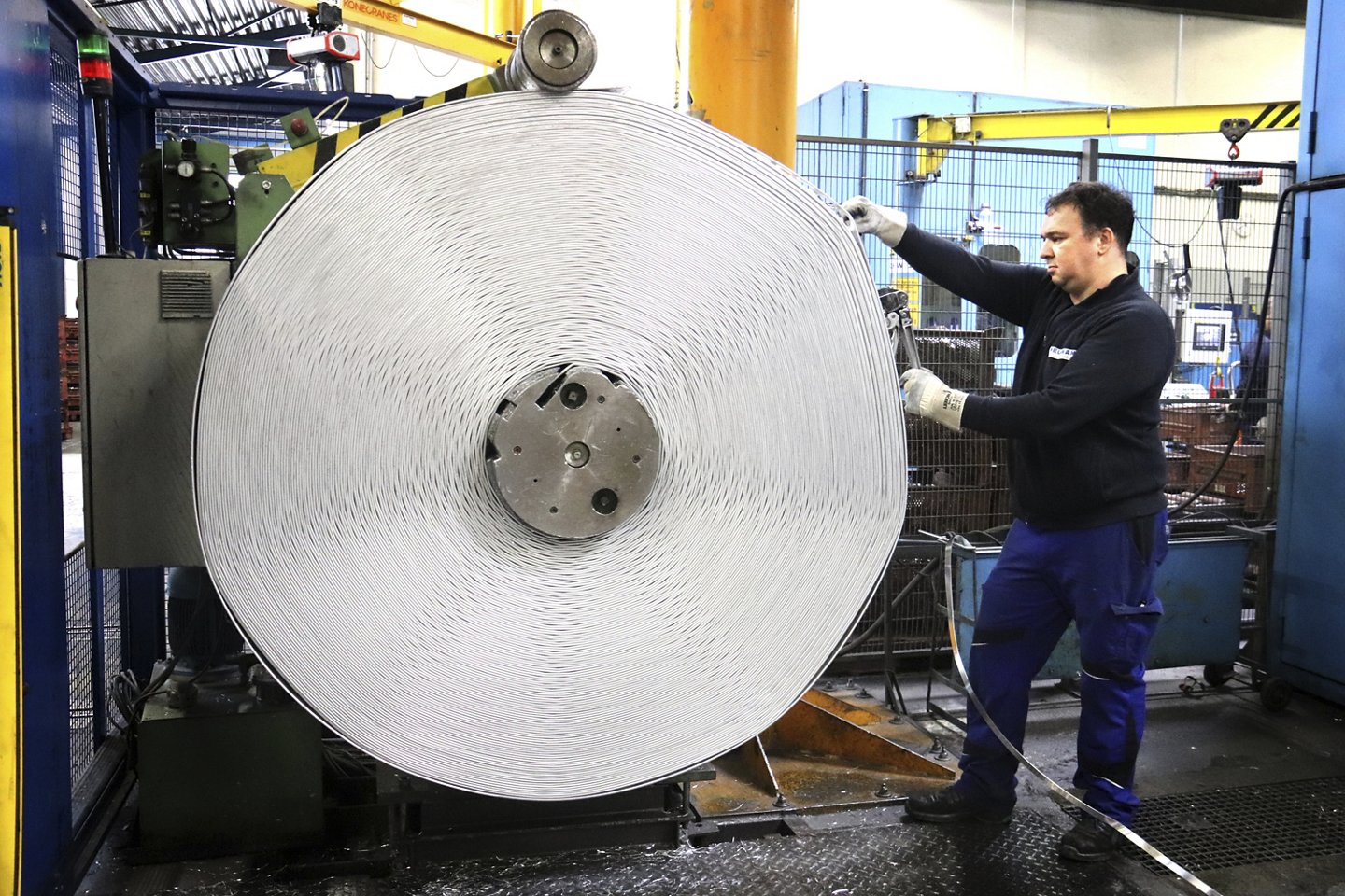 Ein Arbeiter steht an einer Maschine und hält das Ende des Aluminiumbandes, das gerade aufgerollt wird.