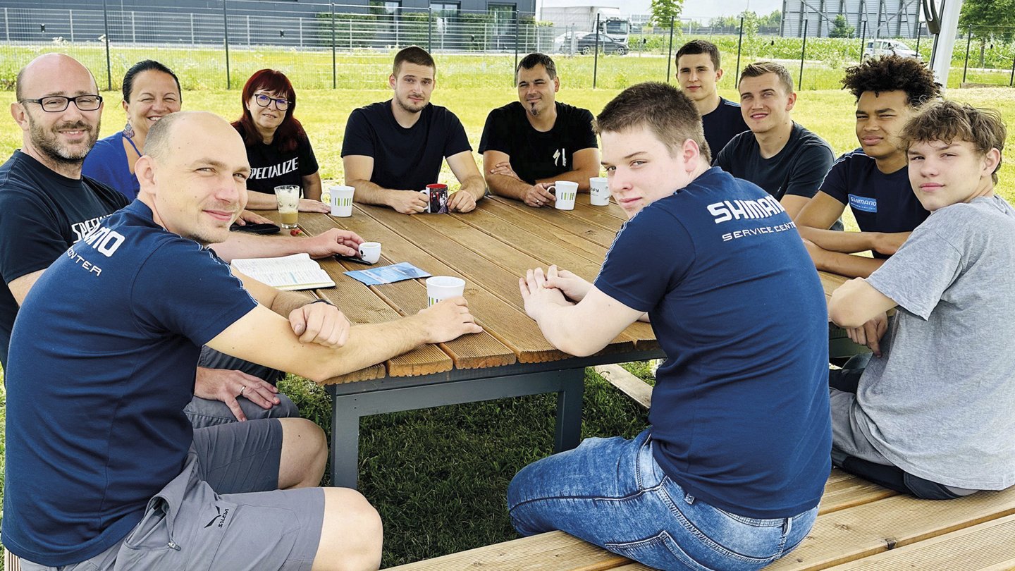 eine Gruppe von Menschen an einem Tisch mit einem Schirm darüber, sie blicken in die Kamera