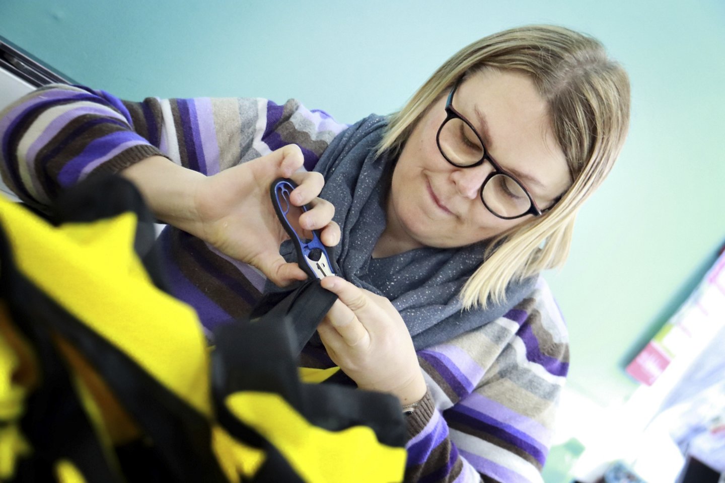 Frau mit Brille und langen, hellen Haaren schneidet mit einem Cutter an einer Fahne.