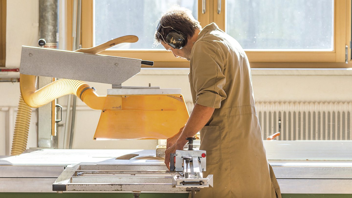 ein Mann mit Gehörschutz steht an einer Schneidemaschine mit Absaugvorrichtung