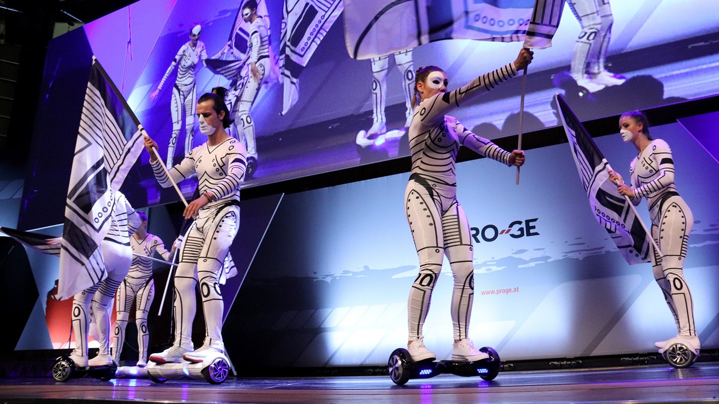 Bühnenchoreografie bei der Eröffnung, Tänzer:innen auf Hoverboards mit Fahnen und weiß-schwarzen Anzügen