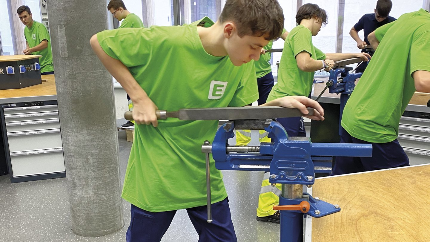 ein junger Mann arbeitet in einer Werkstätte und feilt ein Stück Metall