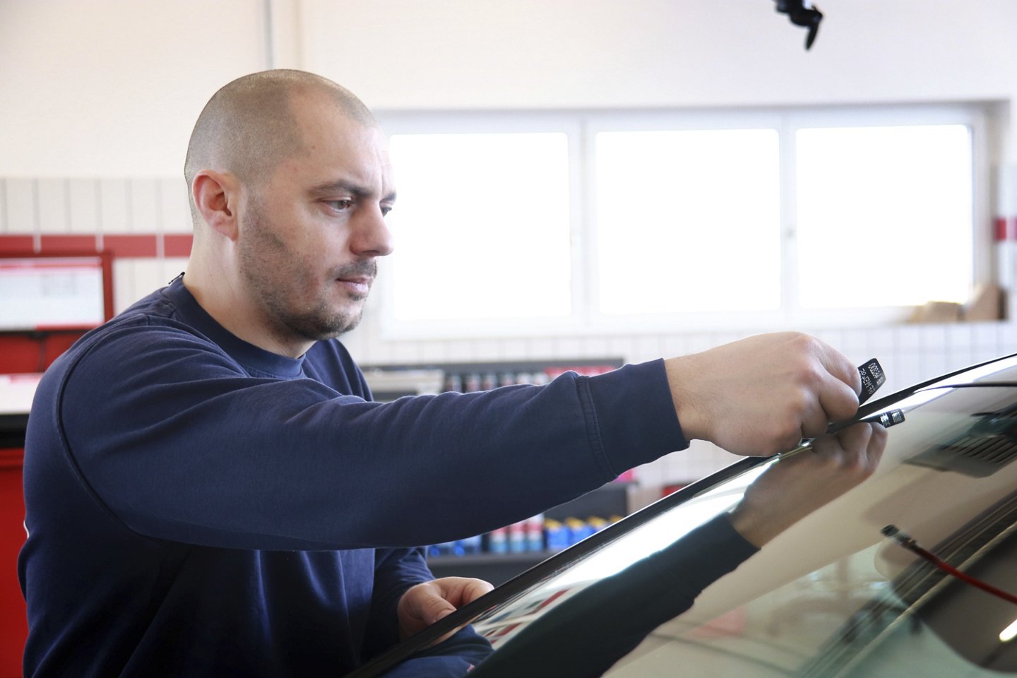 Arbeiter klebt Plakette auf die Windschutzscheibe eines Autos.