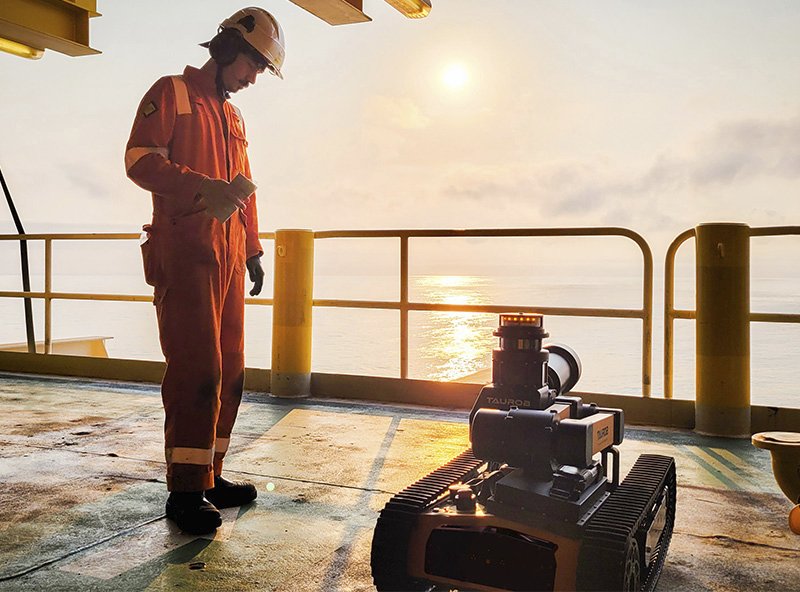 Techniker in Schutzausrüstung beobachtet einen Inspektionsroboter auf einer Offshore-Plattform