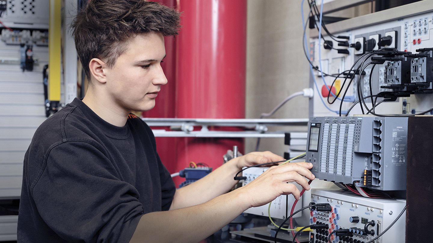 ein Jugendlicher arbeitet an elektronischen Geräten, die mit verschiedenen Steckern miteinander verbunden sind.