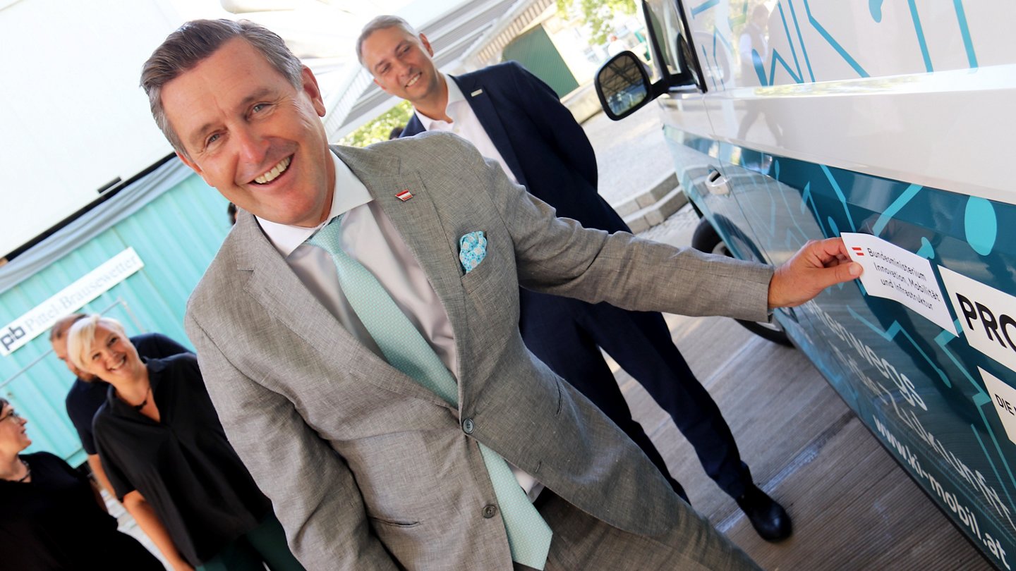 Minister Hanke klebt einen Sticker mit Schriftmarke des Ministeriums auf das KI-Mobil Austria