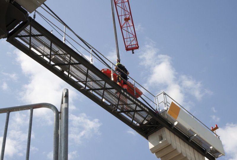 Arbeiter mit Sicherheitsausrüstung arbeitet hoch oben auf einer Brückenkonstruktion unter freiem Himmel.