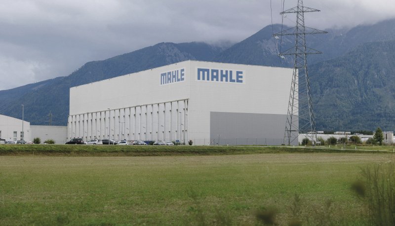 Großes Industriegebäude mit der Aufschrift „Mahle“ vor einer Bergkulisse.