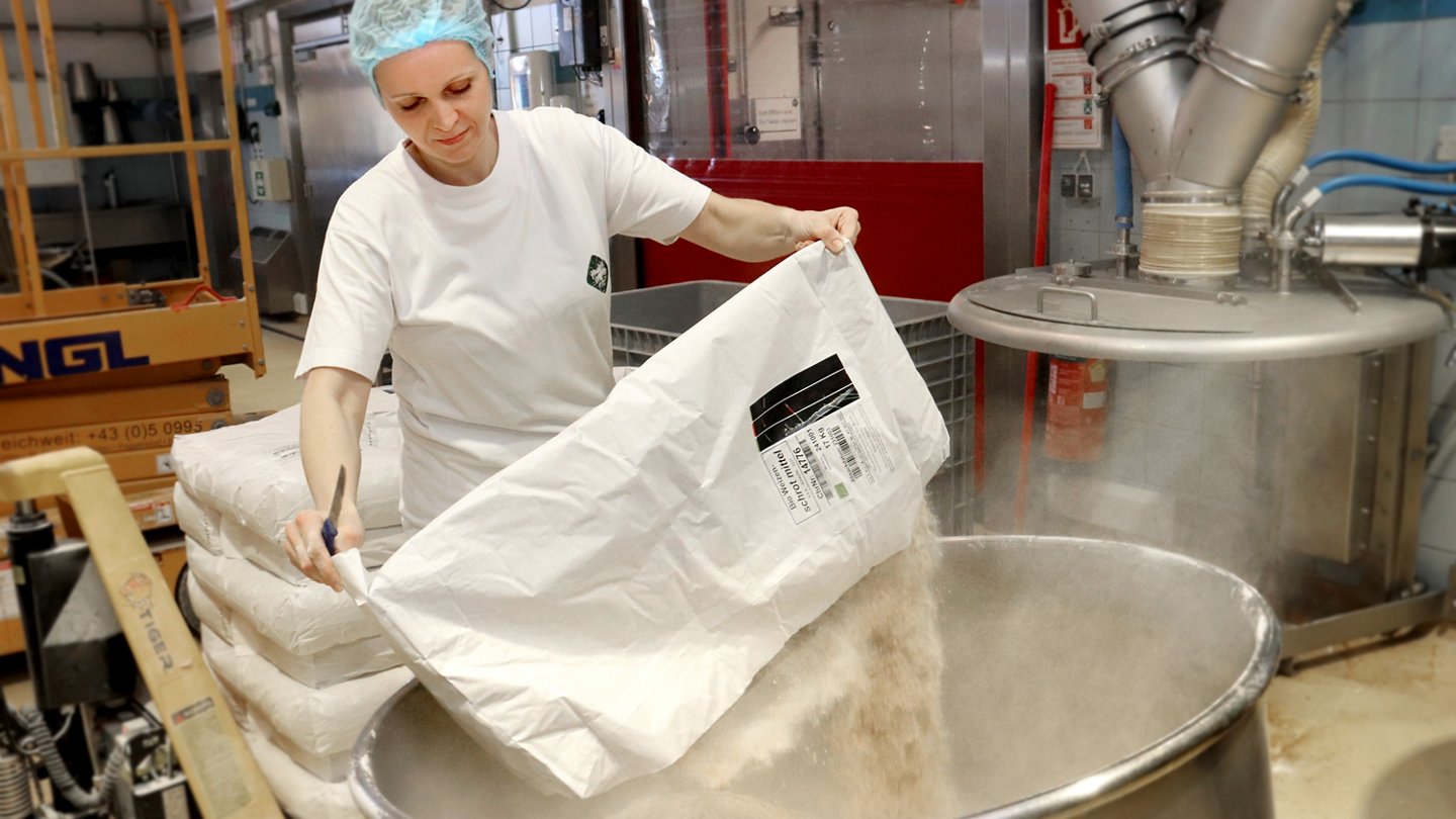 Arbeiterin leert Mehlsack in großen Bottich.