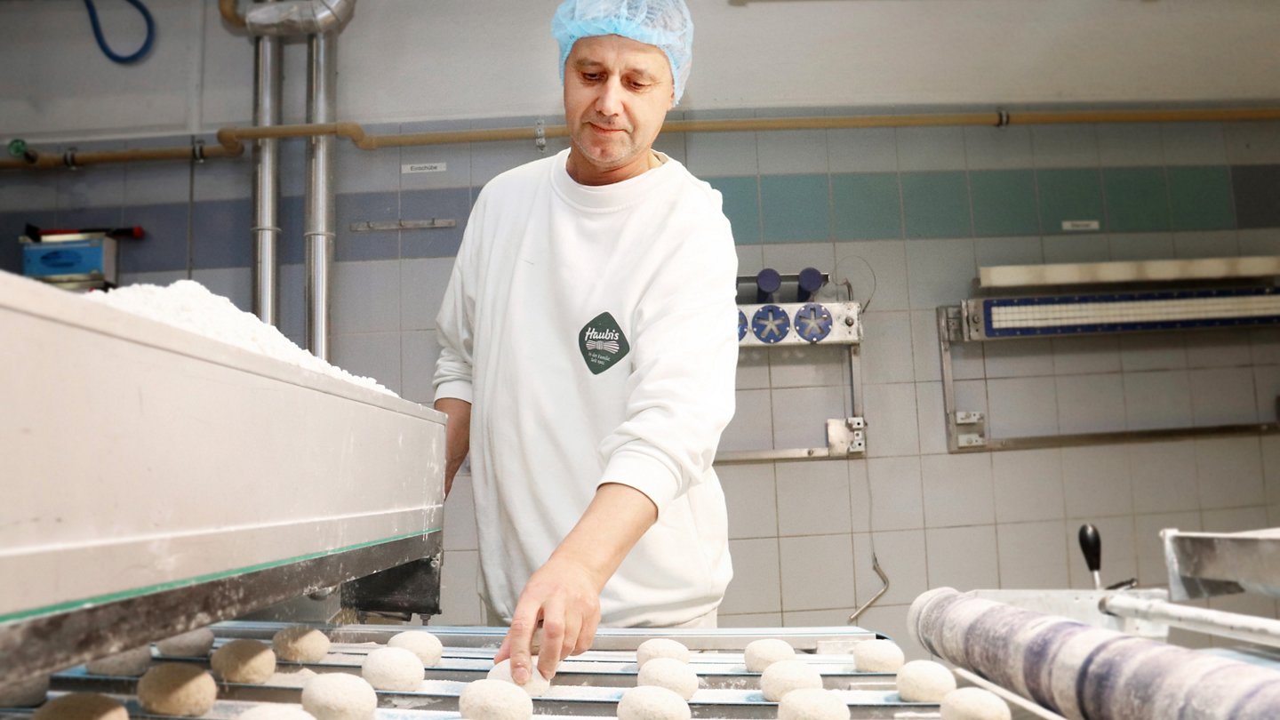 Arbeiter kontrolliert maschinell portionierte Teigstücke.