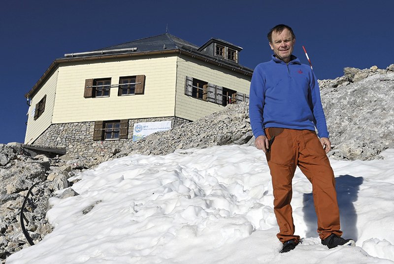 der Hüttenwirt im Schnee vor seiner Hütte