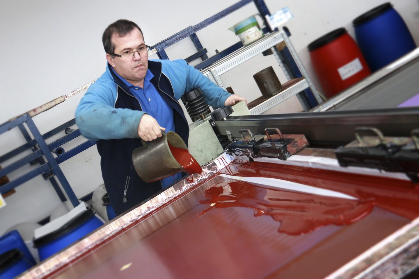 Mann gießt rote Farbe in eine Siebdruckmaschine