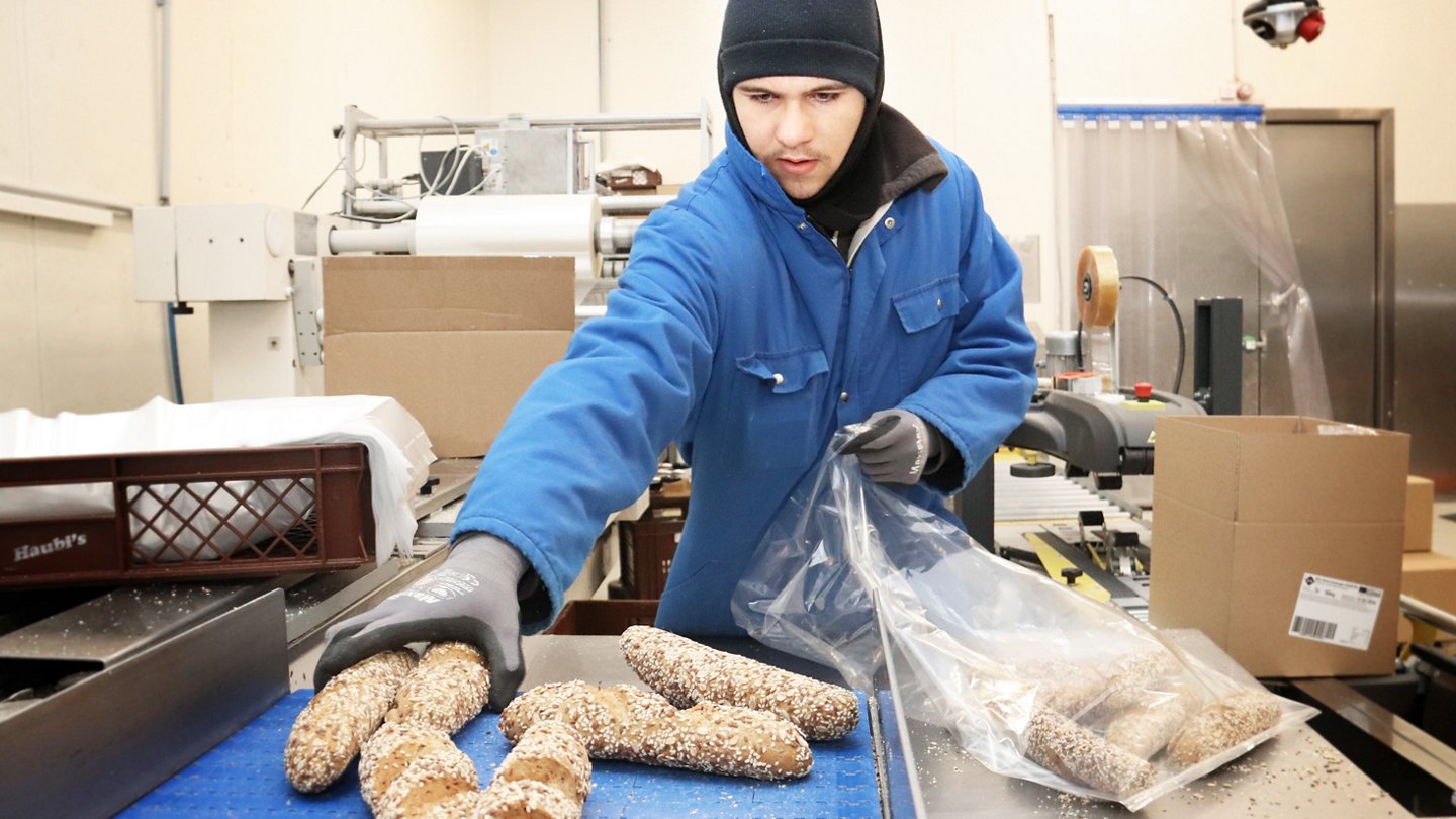 Arbeiter in wärmender Kleidung packt tiefgefrorenes Gebäck in Sackerl..