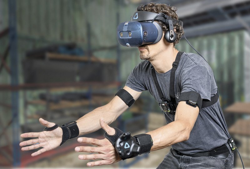 Ein Mann trägt ein Virtual-Reality-Headset und ist mit Sensoren an Armen, Händen und Oberkörper ausgestattet. Diese Technologie ermöglicht das Aufzeichnen und Feedback von Bewegungen, beispielsweise für Schulungen oder ergonomische Untersuchungen.