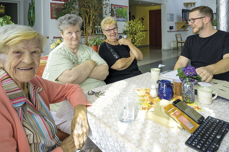 mehrere Seniorinnen sitzen an einem Tisch zusammen, daneben die Sicherheitsfachkraft