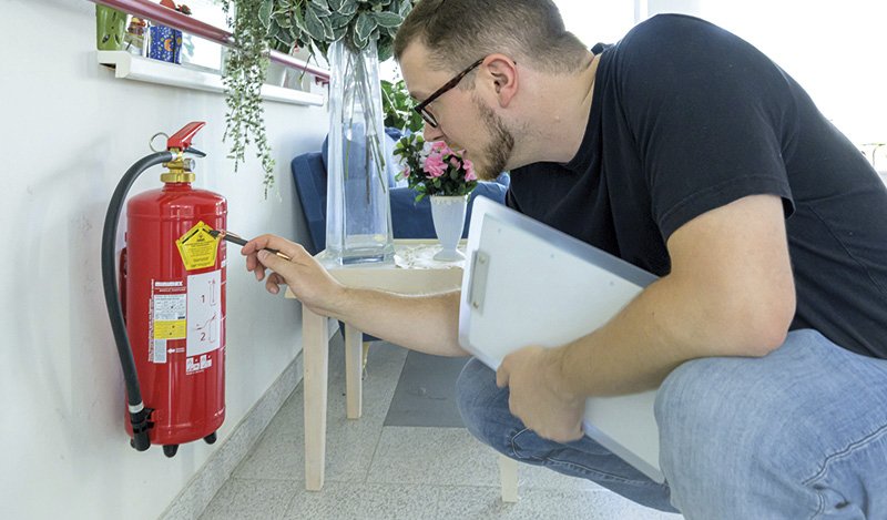 ein Mann begutachtet die Plakette eines Feuerlöschers