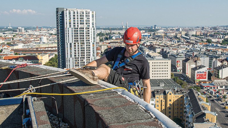 ein Kletterer lässt sich gerade über eine Dachkante hinunter, im Hintergrund sieht man die Stadt